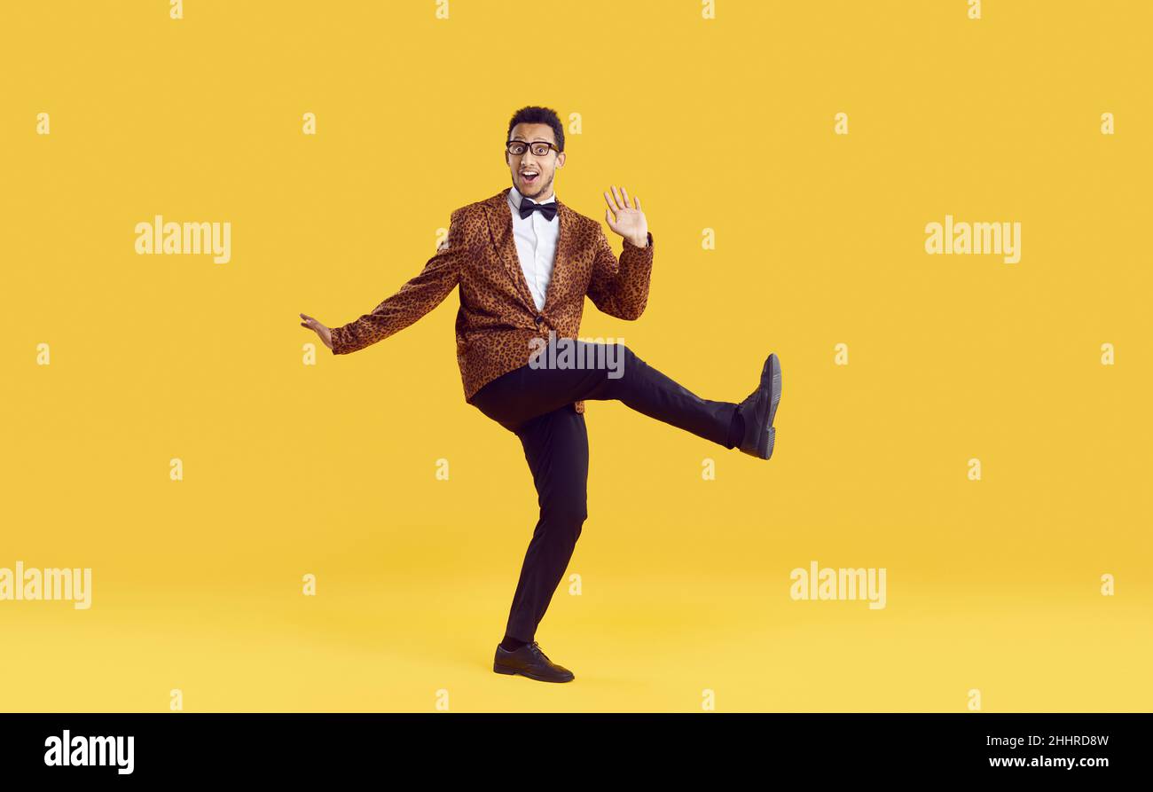 Happy goofy young man in leopard jacket dancing and having fun on yellow background Stock Photo
