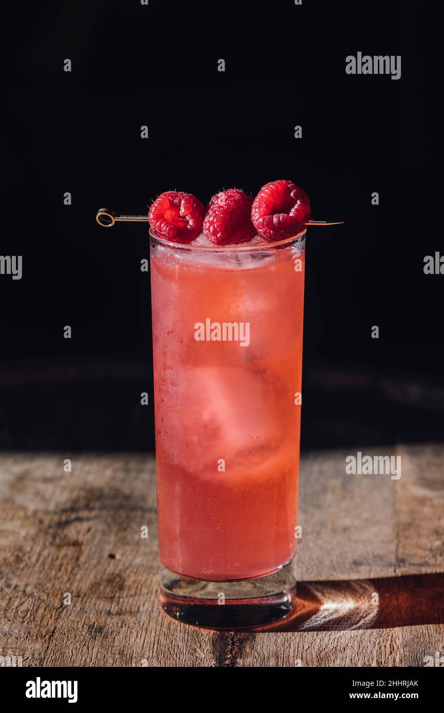 tall pink cocktail drink with three raspberries on cocktail pick, on ...