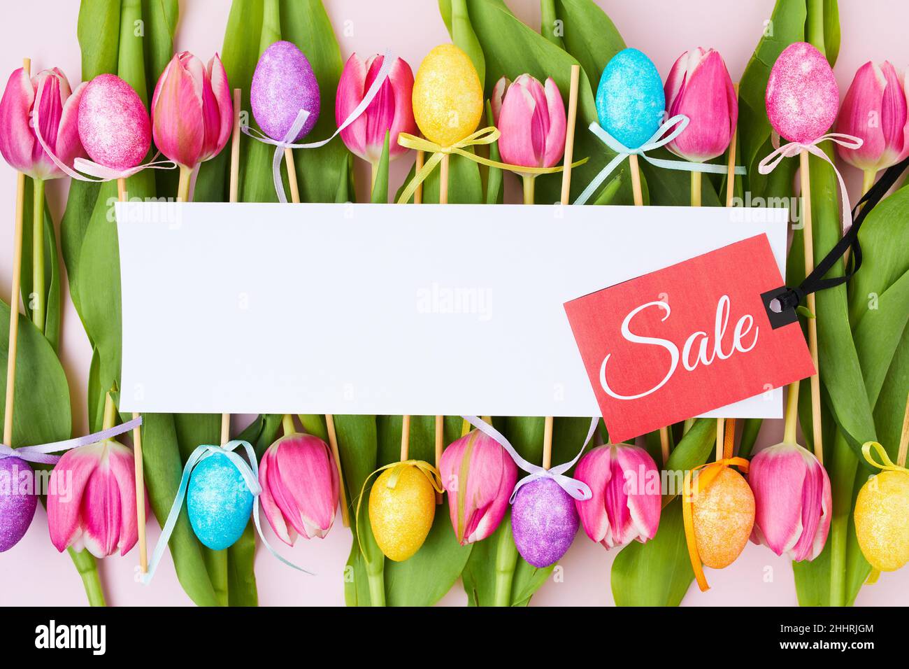 spring flat lay with sale label, paper sheet, tulips and easter eggs isolated on pink background. Stock Photo