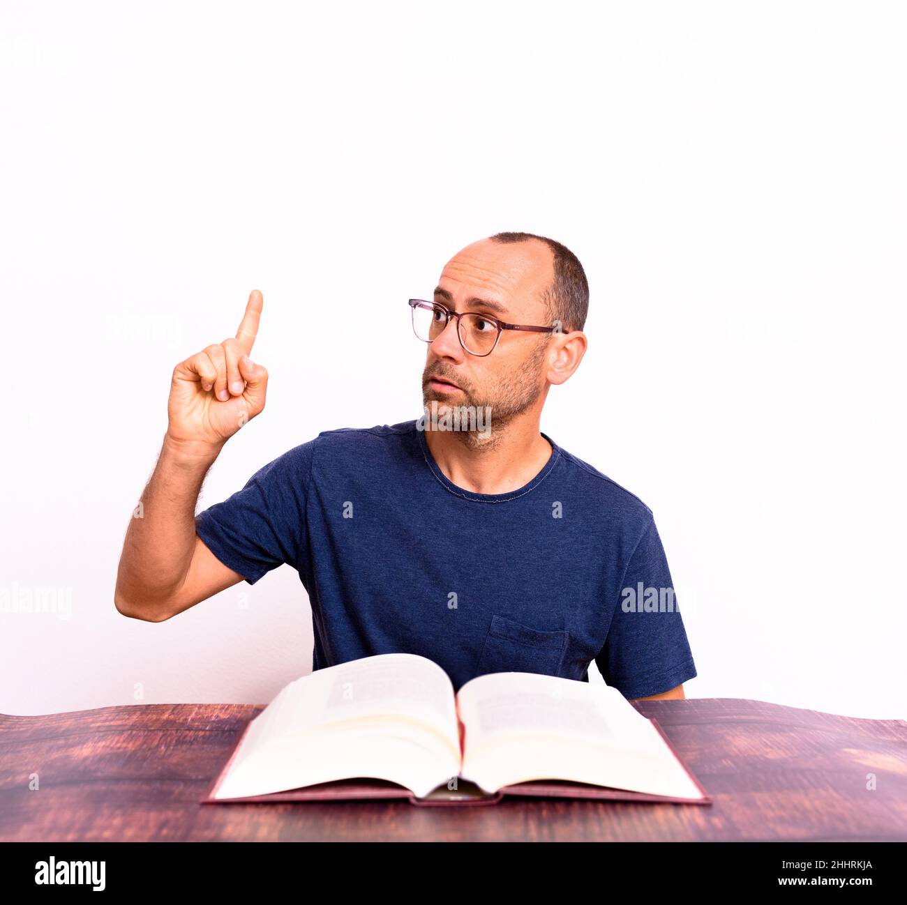 Happy mature man finding the solution to what he was looking for in a book pointing with his finger, isolated on background. Stock Photo