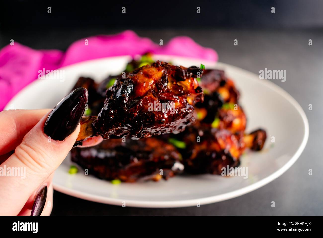 Hand Holding Up a Sticky Glazed Chicken Wing Drumette Closeup view of