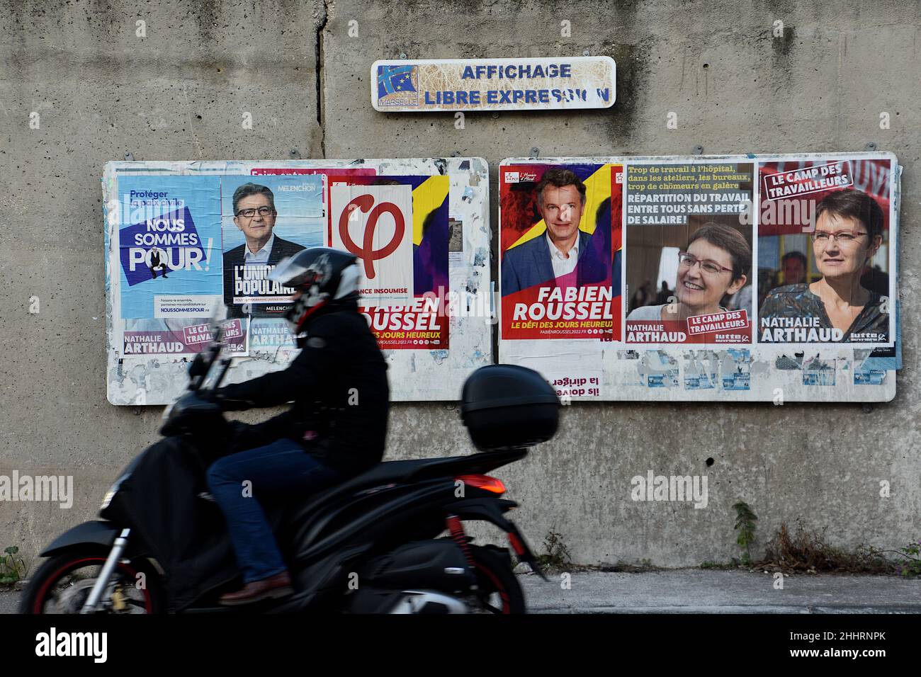 Marseille, France. 25th Jan, 2022. A man on a scooter rides past posters of Jean-Luc Mélenchon (L), Fabien Roussel (C) and Nathalie Arthaud (R) on display.Posters campaign of Nathalie Arthaud, Fabien Roussel, Philippe Poutou and Jean-Luc Mélenchon, candidates for the French presidential elections of 2022. Credit: SOPA Images Limited/Alamy Live News Stock Photo