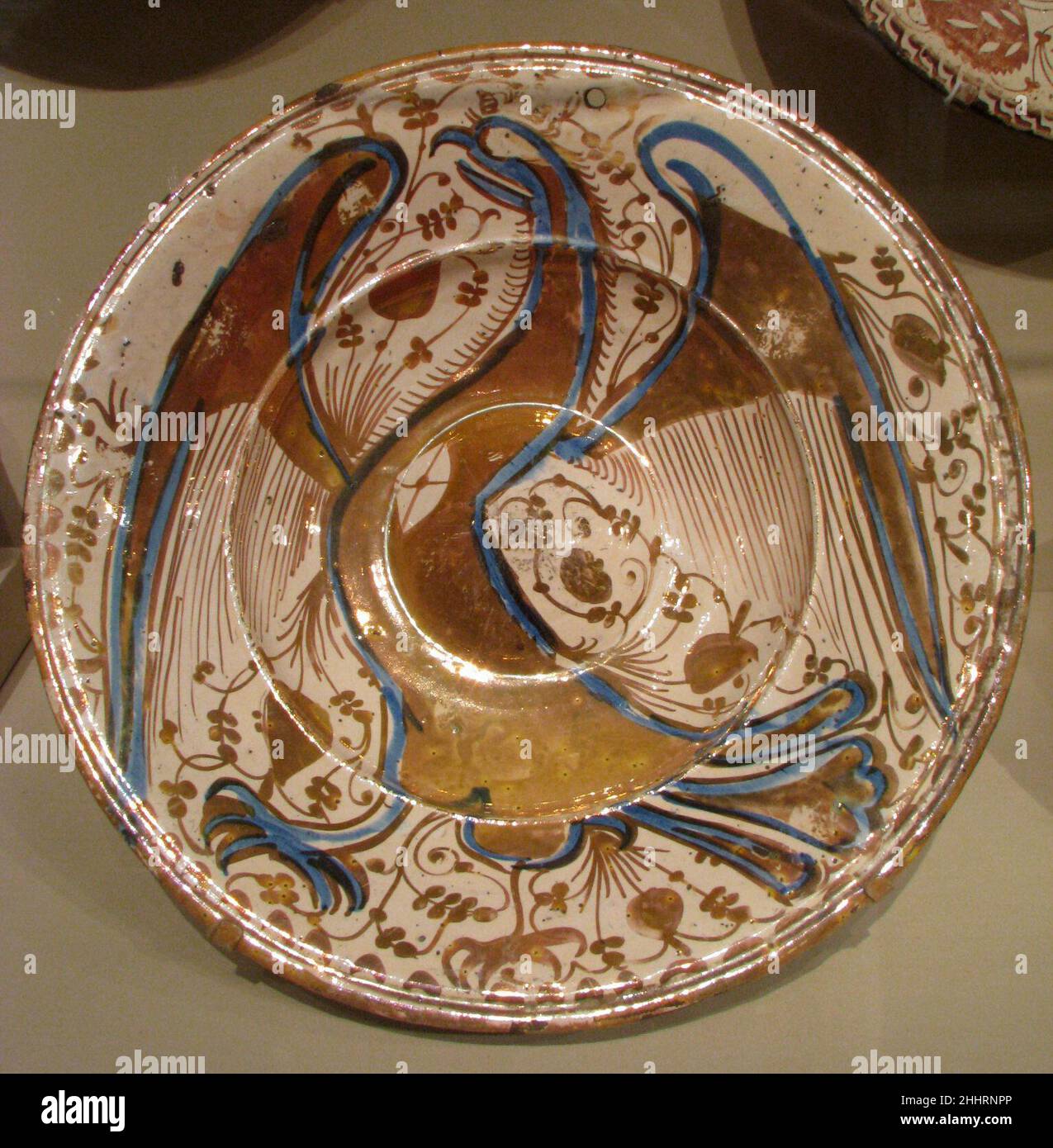 Dish late 16th–early 17th century Spanish, Valencia The free and confident draftsmanship of the eagle as well as the loose style of the leafy tendrils in the background are typical of the late sixteenth century. The edging of arcs around the border belongs to the a l'ungla ('with the fingernail') style.. Dish. Spanish, Valencia. late 16th–early 17th century. Tin-glazed and luster-painted earthenware. Ceramics-Pottery Stock Photo