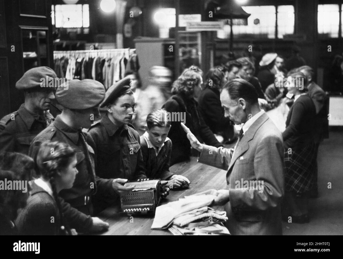 Bombadier Tom Burridge of Deptfprd, London and his comrade Bombadier Poppleseell of Middlesbrough attempt to trade their cigarette lighter  for an accordion at a barter exchange in Luneburg, Germany after the Second World War. After the war there was  a scarcity of vital necessities such as food, clothing and every day commodities such as appliances and household utensils. As none of these were being manufactured the only option left to Germans to acquire these things was through a trade barter. Stock Photo