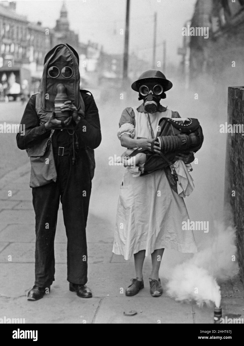 Air raid warden with nurse and baby in arms seen demonstrating the new gas helmet during an air raid gas exercise on Merseyside 24th July 1941 Stock Photo