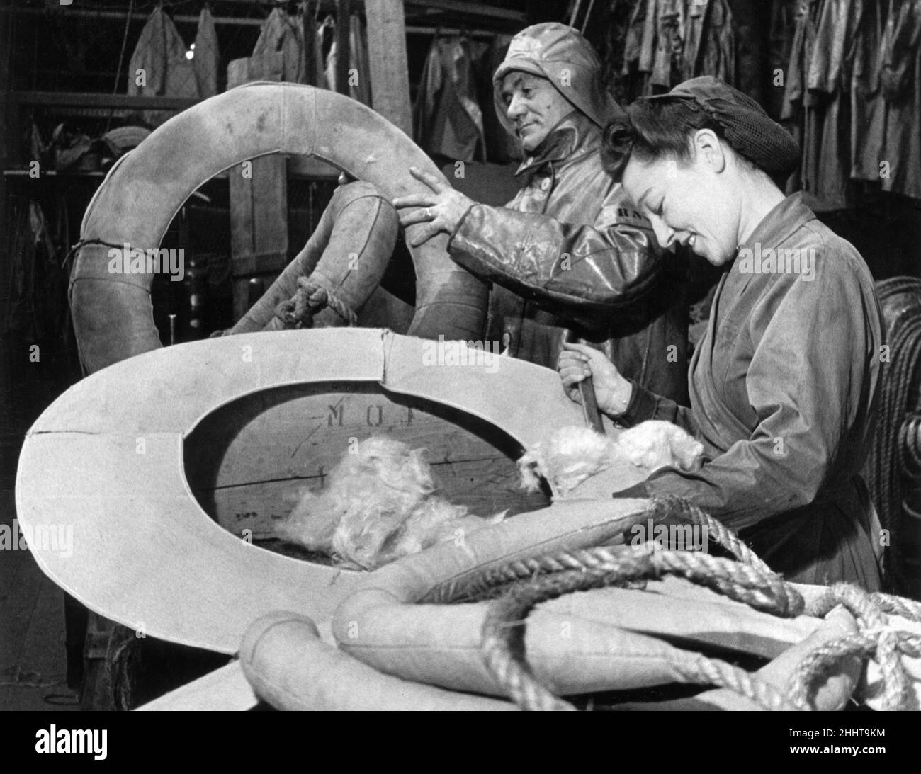 Miss Vera Pearson helping in the rigging loft of the Royal National Lifeboat Institutions Stores. Alfred Stephens, an ex-Navy man, is teaching her to fix a thimble to a six inch rope and the filling of lifebouys with Kapok. The rigging loft is stored with coils of stout rope for issue to coastal crews.28th December 1944. Stock Photo