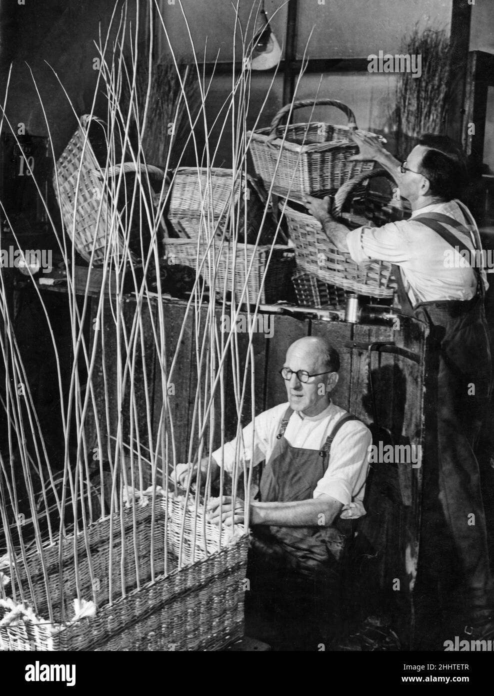 Wil Preedy sits cross legged making a hamper basket while his brother Arthur sorts out some of the finished articles in their Deritend workshop. 21st May 1952 Stock Photo