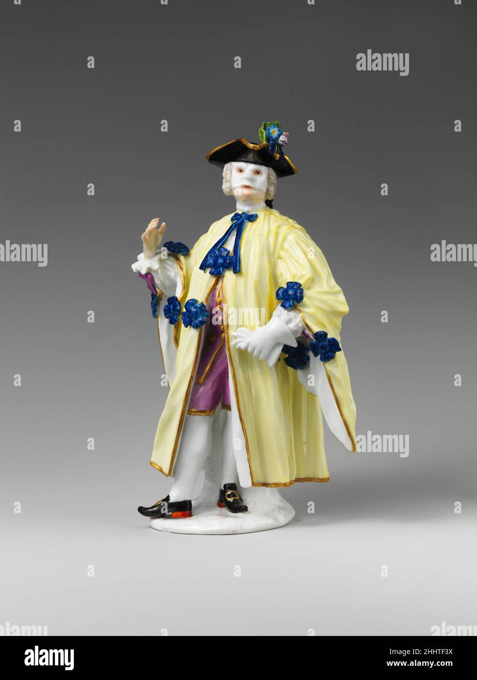 Masquerader (one of a pair) 1745 Meissen Manufactory German This model of a porcelain figure wearing a black tricorne hat, a white half mask, and a long robe trimmed with bows is commonly identified as the Avvocato, or lawyer, one of the secondary cast of characters comprising the Comédie Italienne. However, it has been pointed out recently that neither the costume nor the pose of this figure refers to the legal profession and that the figure should more accurately be called 'The Masquerader.'[1] His hat, mask, and cloak reflect a costume typically worn by both men and women in Venice during C Stock Photo