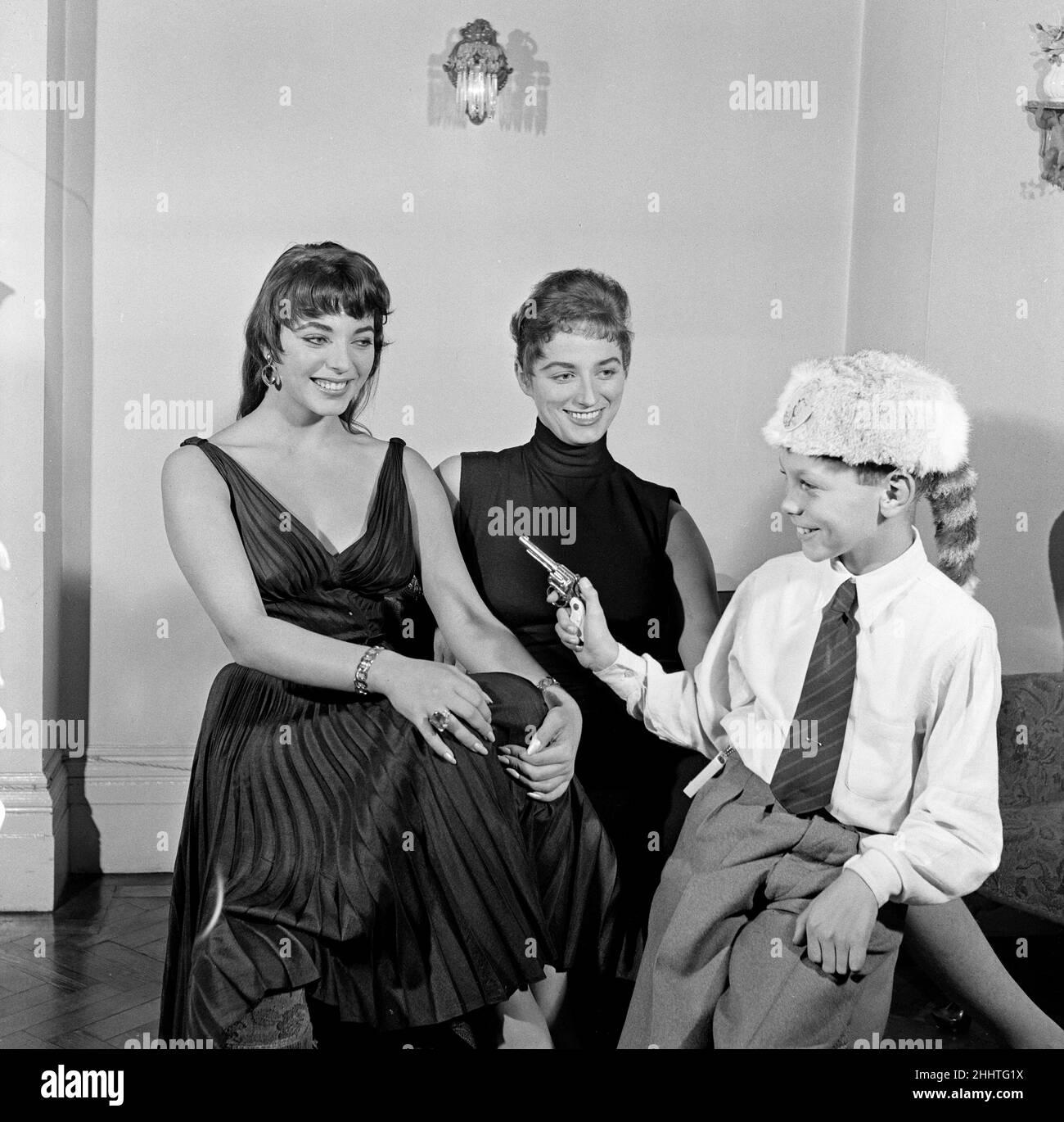 Joan Collins, actress, aged 22, pictured wearing black silk cocktail dress, at her flat in Marylebone, London, 10th February 1954. Photo-call after 10 months stay in Hollywood. Pictured with younger sister Jackie Collins and brother Bill Collins, wearing Davy Crockett hat. Stock Photo