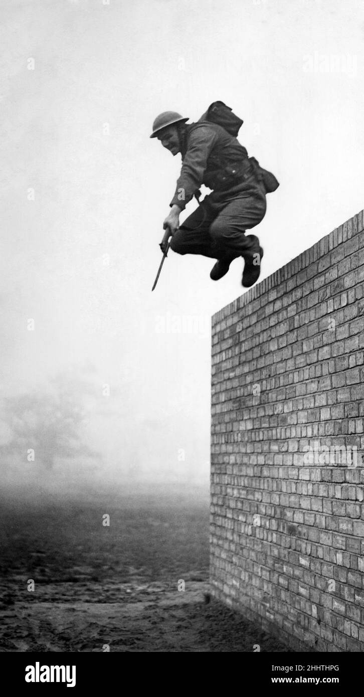 World war II Army: Here is the tallest man at the Infantry Training School, Western Command. He is Cow Puncher Eddie Hookings, aged 21, from Canada, He is jumping from a 10ft wall and he is nearly 7ft high. November 1942 P014907 Stock Photo
