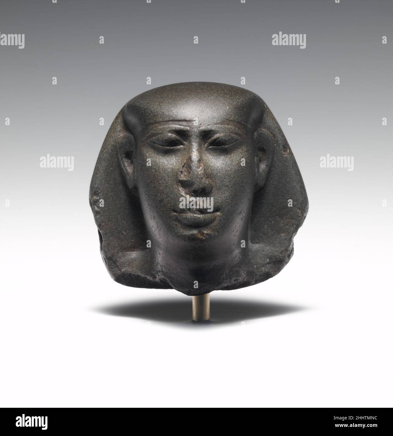 Head of King Amasis, reworked for a non-royal individual 570–526 B.C. Late Period, Saite The bag wig now visible betrays the original form of the royal nemes headdress, indicating this head was recut from a royal portrait for a non-royal official. The long face and high-set brow line are distinctive characteristics of King Amasis, indicating this sovereign was originally represented.. Head of King Amasis, reworked for a non-royal individual  553275 Stock Photo