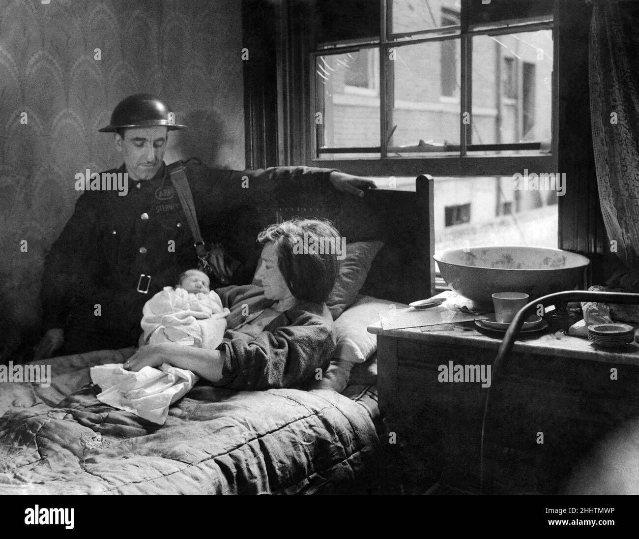 Warden Bill Watson at the bedside of Mrs. R. Foster. With bombs fallinground, as Mrs. Foster lay on that bed in darkness, and shattered glass, Mr. Watson acted as midwife at the unexpected birth of her child during the first large scale air raid on London. 8th September 1940 Stock Photo