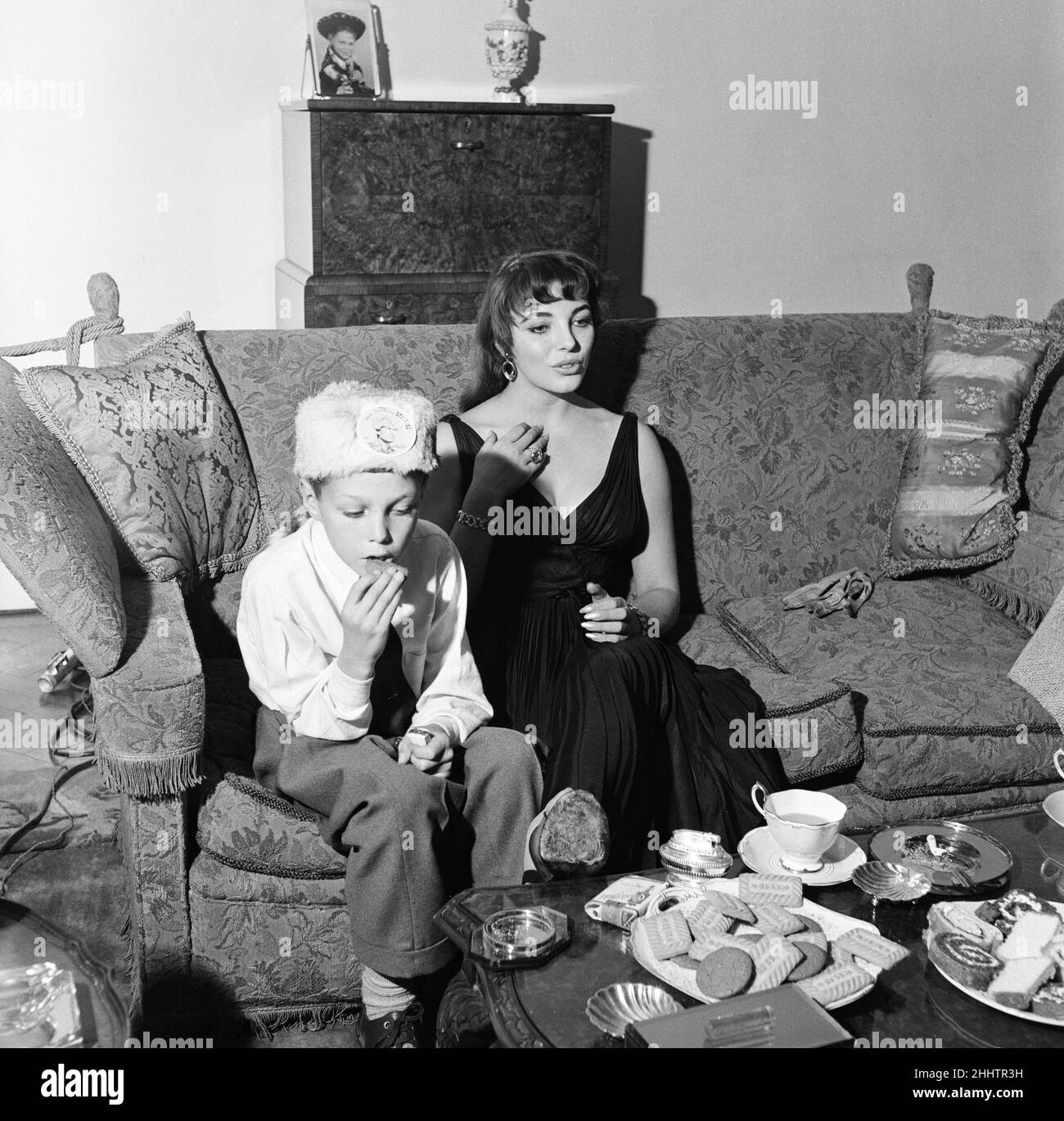 Joan Collins, actress, aged 22, pictured wearing black silk cocktail dress, at her flat in Marylebone, London, 10th February 1954. Photo-call after 10 months stay in Hollywood. Pictured with younger brother Bill Collins, wearing Davy Crockett hat. Stock Photo