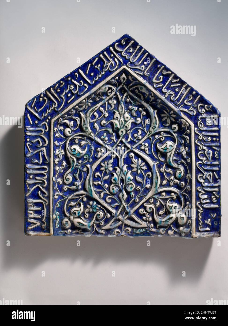 Tile from a Mihrab dated A.H. 722/ A.D. 1322–23 This tile once formed part of a mihrab, or niche, facing Mecca, toward which prayer is directed in mosques. The inscription at its top includes a Qur'anic reference to the mihrab’s function, and provides the date of the tile’s manufacture in the fourteenth century. This surrounds the modeled vine and tendril motif executed with touches of black and turquoise. We must imagine that the interior walls of the building containing this mihrab were once covered in similar tiles, as was common during the Ilkhanid period in Iran.. Tile from a Mihrab. date Stock Photo