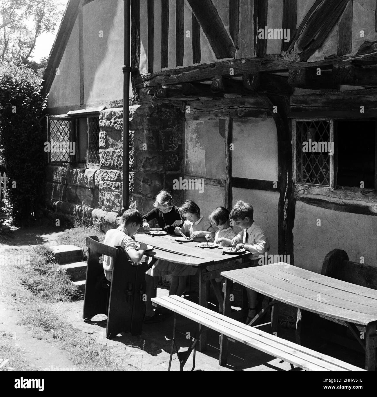 In the Pilgrims Rest, the ancient Tudor looking hostelry outside the Battle Castle are 5 children having their school meal. They and their school mates have their school meal there every day. Left to right, Jane Goodwin 9, Isabelle de Villier-Guimbieu 8, Mary Taylor 5, David Lovelock 7 and Alexander Wagstaff 9. The children are from the Gay Bows School. Battle, East Sussex, 21st July 1954.In the Pilgrims Rest, the ancient Tudor looking hostelry outside the Battle Castle are 5 children having their school meal. They and their school mates have their school meal there every day. Left to right, J Stock Photo