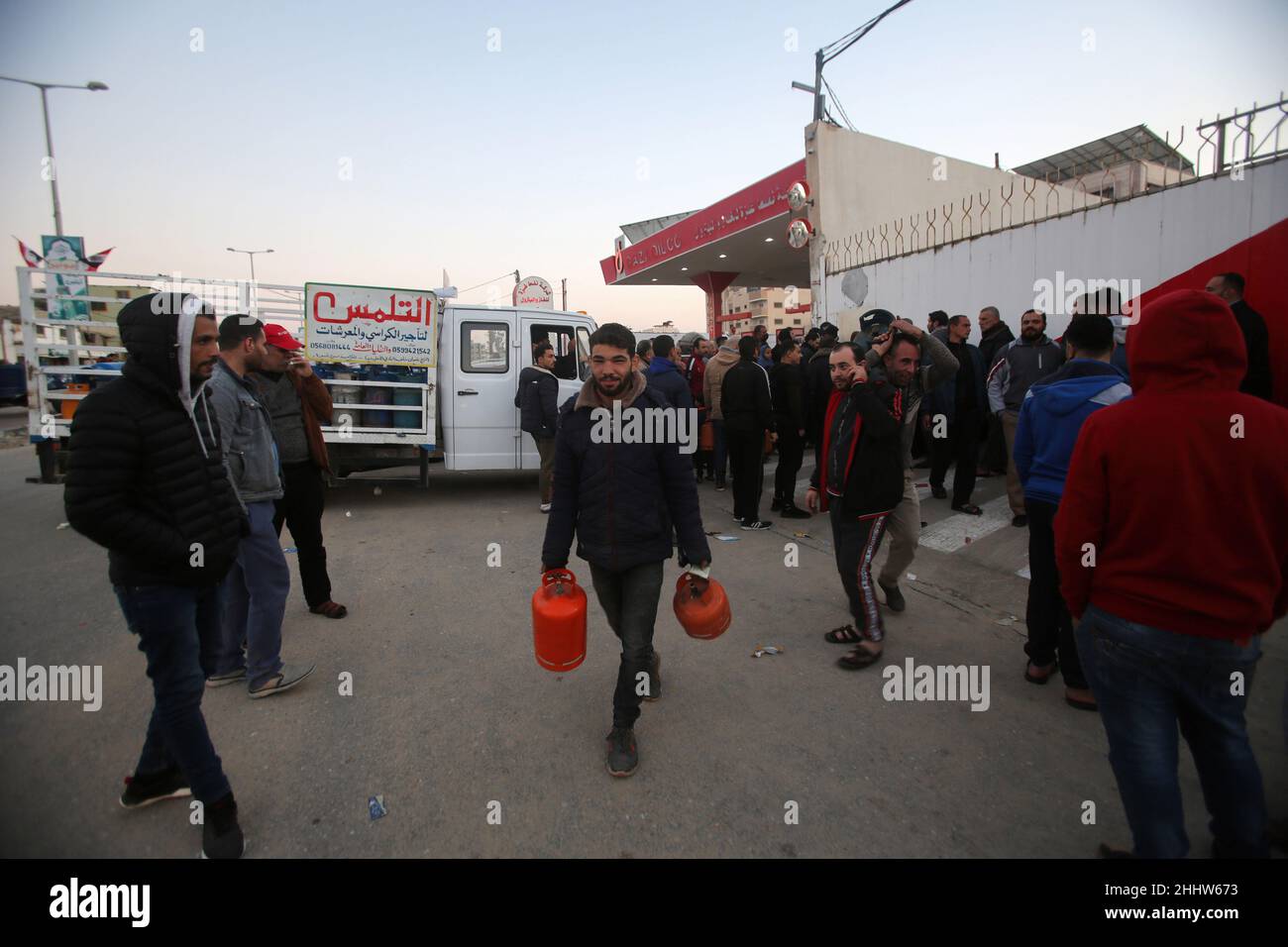 A Palestinian man seen carrying cylinders while smiling after he has filled up his gas cylinders in front of big gas station. Shortage of gas and inability to fill the gas cylinders in their homes, which makes the winter difficult, as gas is one of the sources of heating. The crisis is repeated almost every year at this time as a result of the increasing need for gas, in addition to the lack of a strategic reserve of gas for the owners of the stations, the Gaza strip obtains gas either through the Rafah crossing from Egypt or from the Israeli side. Stock Photo