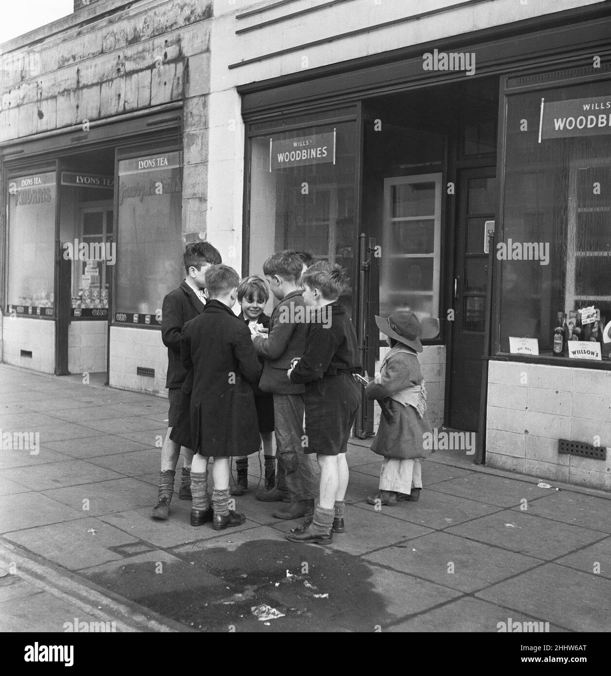 Life in the Mirror Our Gang. 19th January 1954  A gang of boys plot todays agenda of mischief and mayhem outside a tobacconist in Bow Road in the East End of London Mirror Captions: This is The Conference. Not the stiff necked, prim and tight lipped Conference of the Foreign Minister coming off next week in Berlin, but the Conference down OUR street. OUR street being Bow Road, London. Six Kids (some of 'em in sad need of a hair cut) are plotting today's glorious agenda of mischief by boys for boys - including a couple of escapades for the pint sized Mountie and Young Sloppy - Sock there on the Stock Photo
