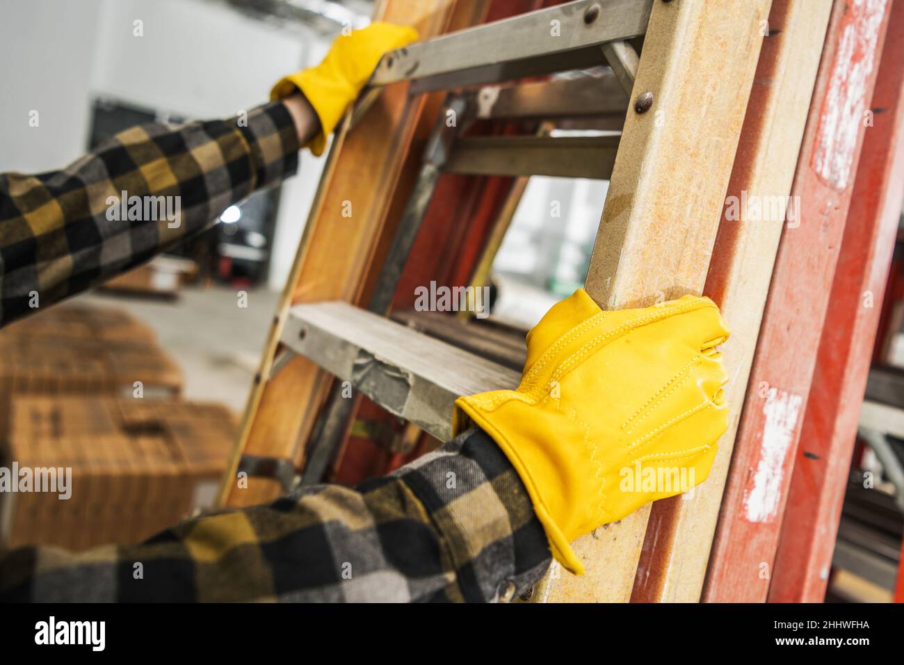 Construction Worker Wearing Safety Gloves Moving Commercial Grade Ladders Within Construction Site. Stock Photo
