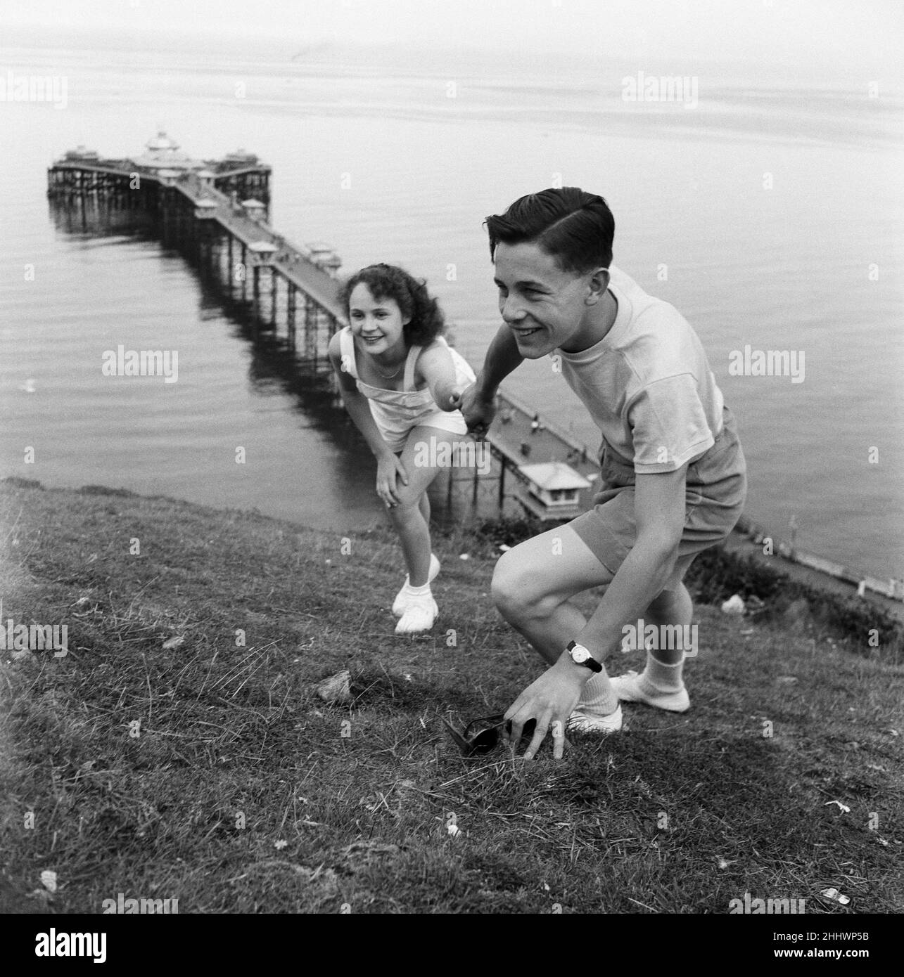 Holiday makers in Llandudno, Conwy County Borough, Clwyd, Wales. A young couple climbing up a hilly bank, with the pier in the background. 22nd August 1949. Stock Photo