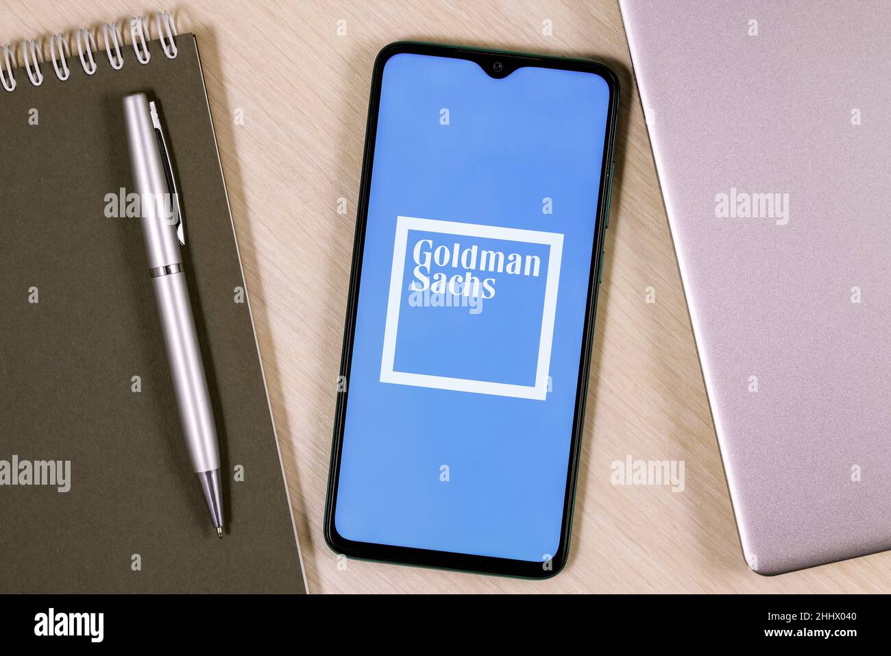 Smartphone with Goldman Sachs bank logo on wooden table next to laptop and business planner Stock Photo