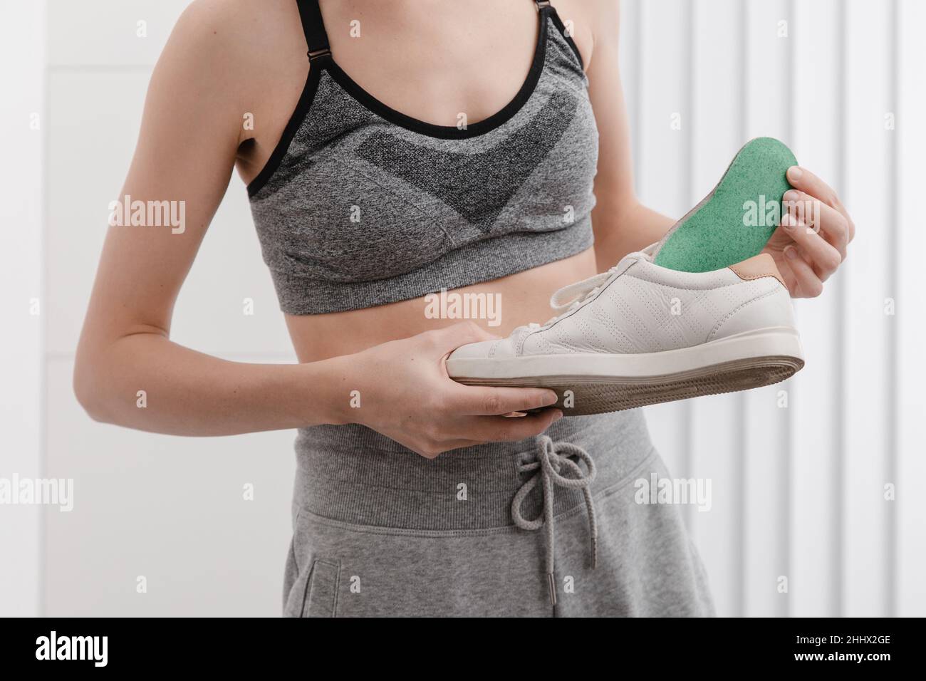 Woman putting orthopedic insole into shoe at home. Sports girl fitting orthopedic insole indoors, close up. Foot care banner. Flat Feet Correction Stock Photo