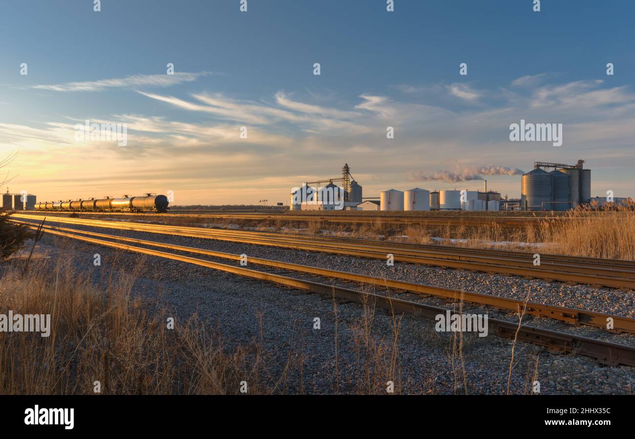 Scenic view of ethanol production facility along a railway with railroad tanker cars lined up at sunsetr. Stock Photo