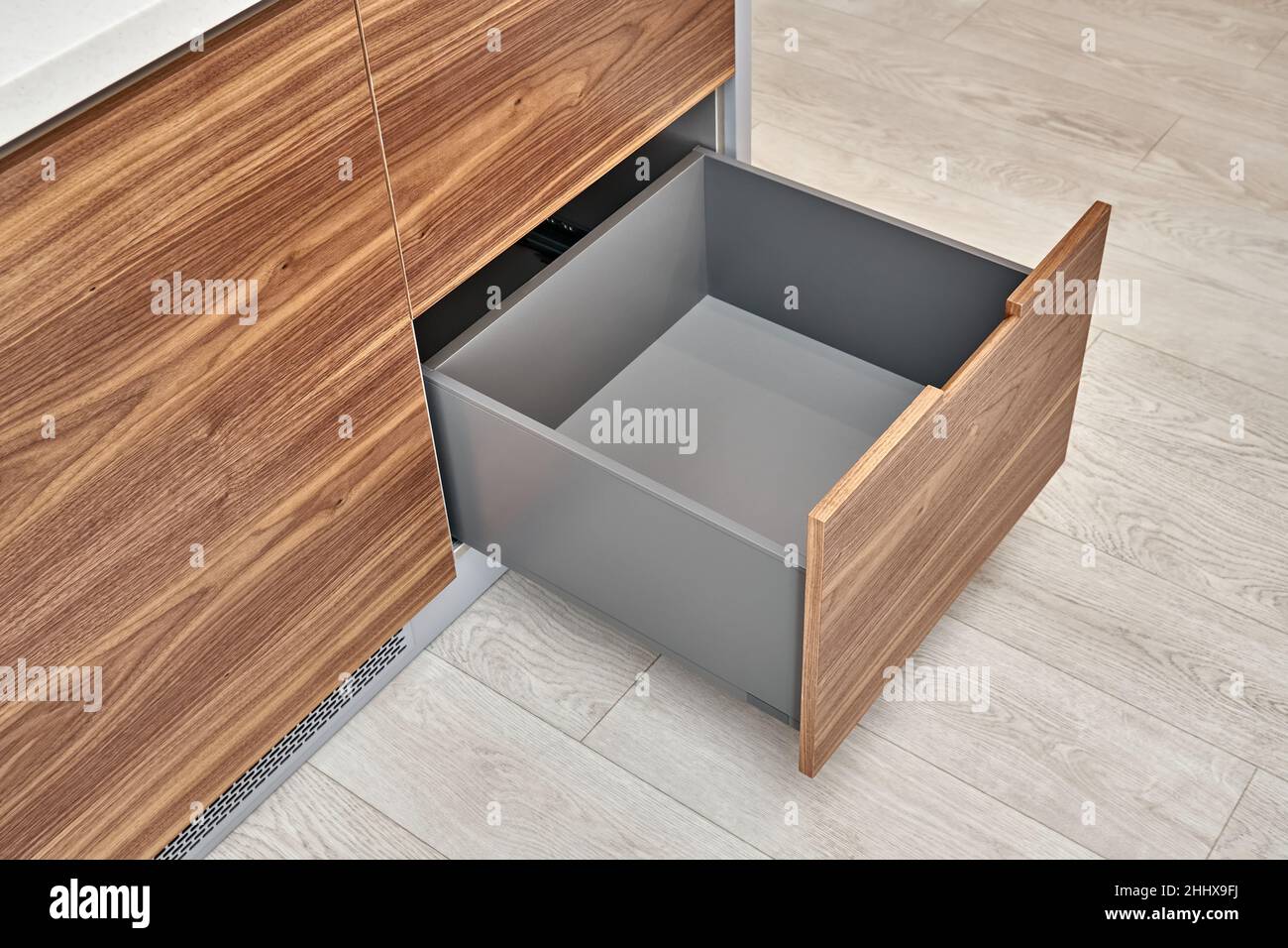 Open lower drawer of dark grey color in contemporary kitchen of walnut wood and gray color with acrylic solid surface countertop close-up Stock Photo