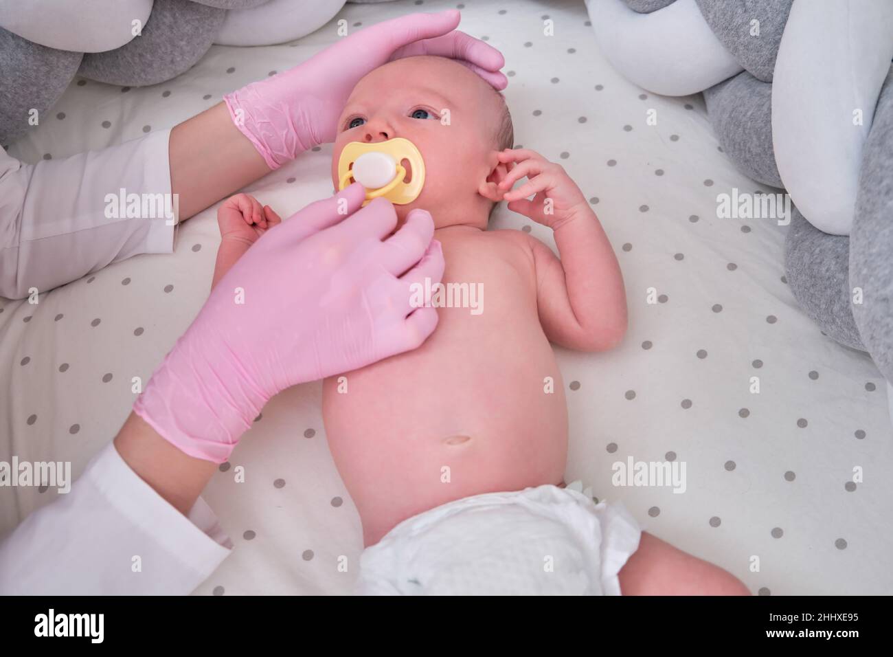The doctor gives a pacifier to a newborn baby. Nurse in uniform soothes
