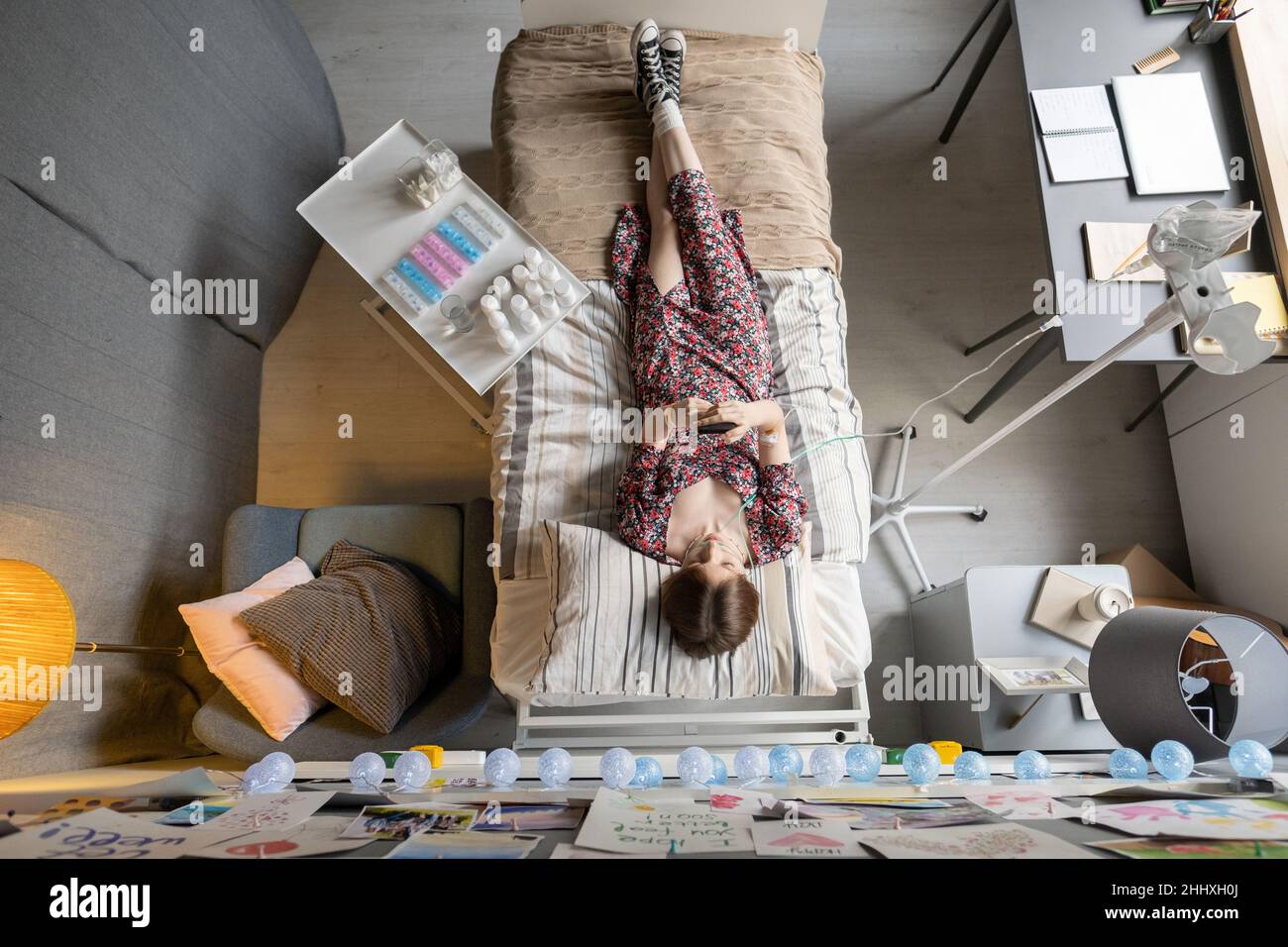 Overview of sick girl with smartphone lying on bed during medical procedure while staying in hospital for intensive therapy course Stock Photo