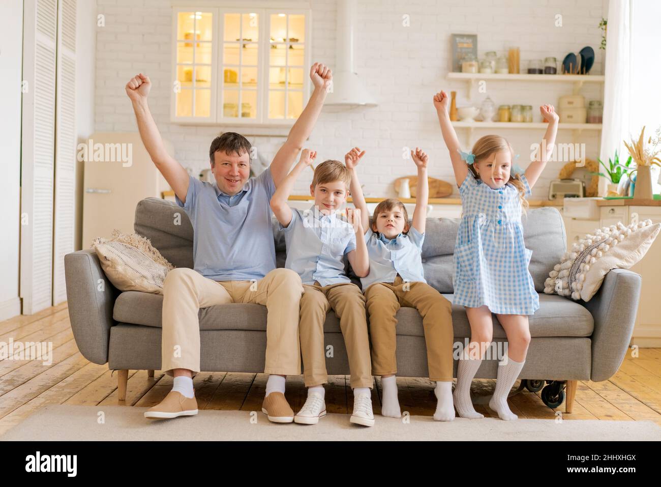 Happy dad and little kids laughing at funny humorous comedy movie or tv show sitting at home on sofa in living room kitchen smiling father having fun with kids watching tv together at weekend Stock Photo