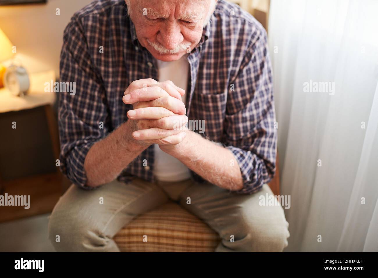 Elderly man with his fingers crossed by his face sitting on chair and