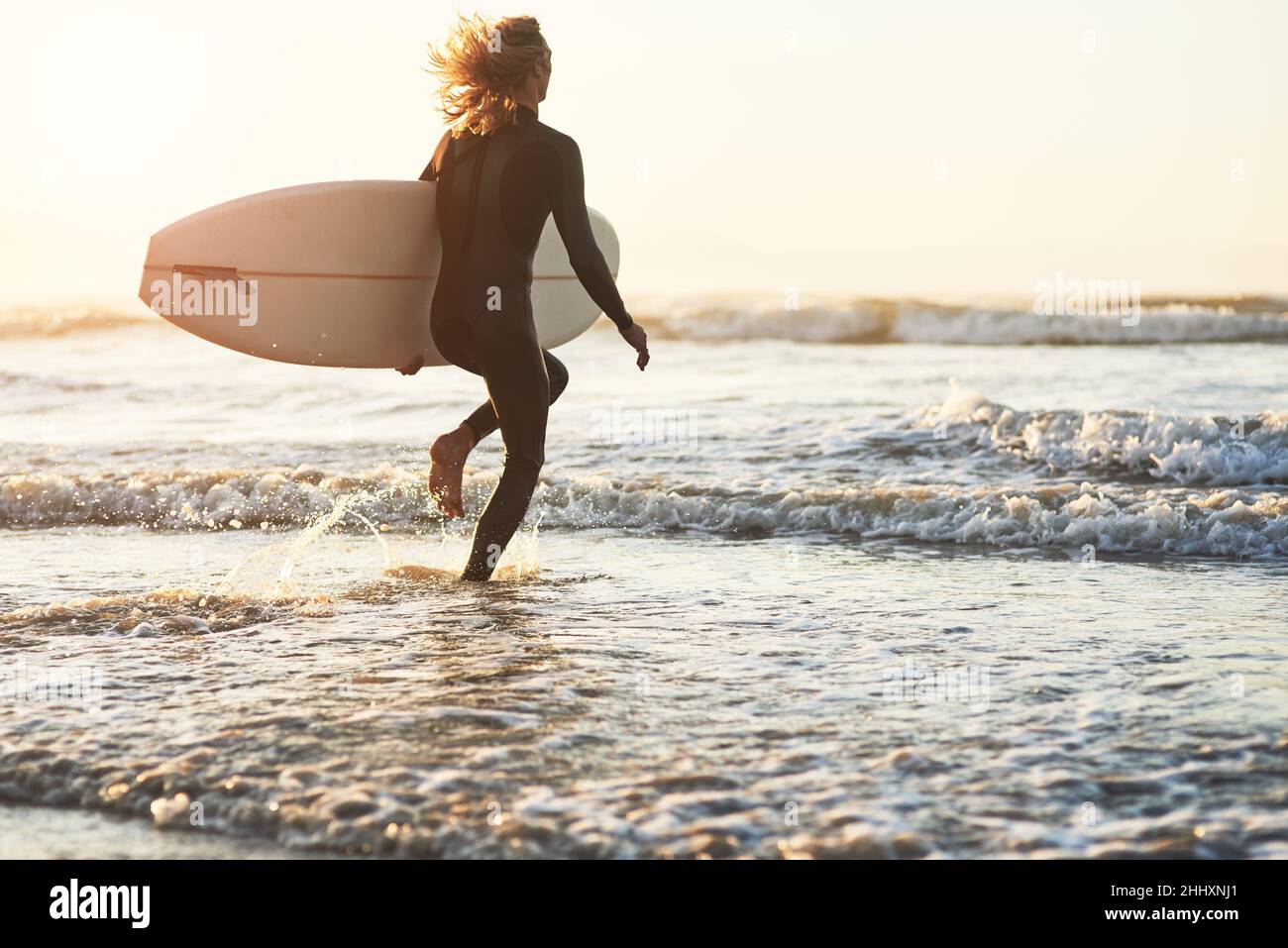 Break free from the world. Rearview shot of a young man surfing at the beach. Stock Photo