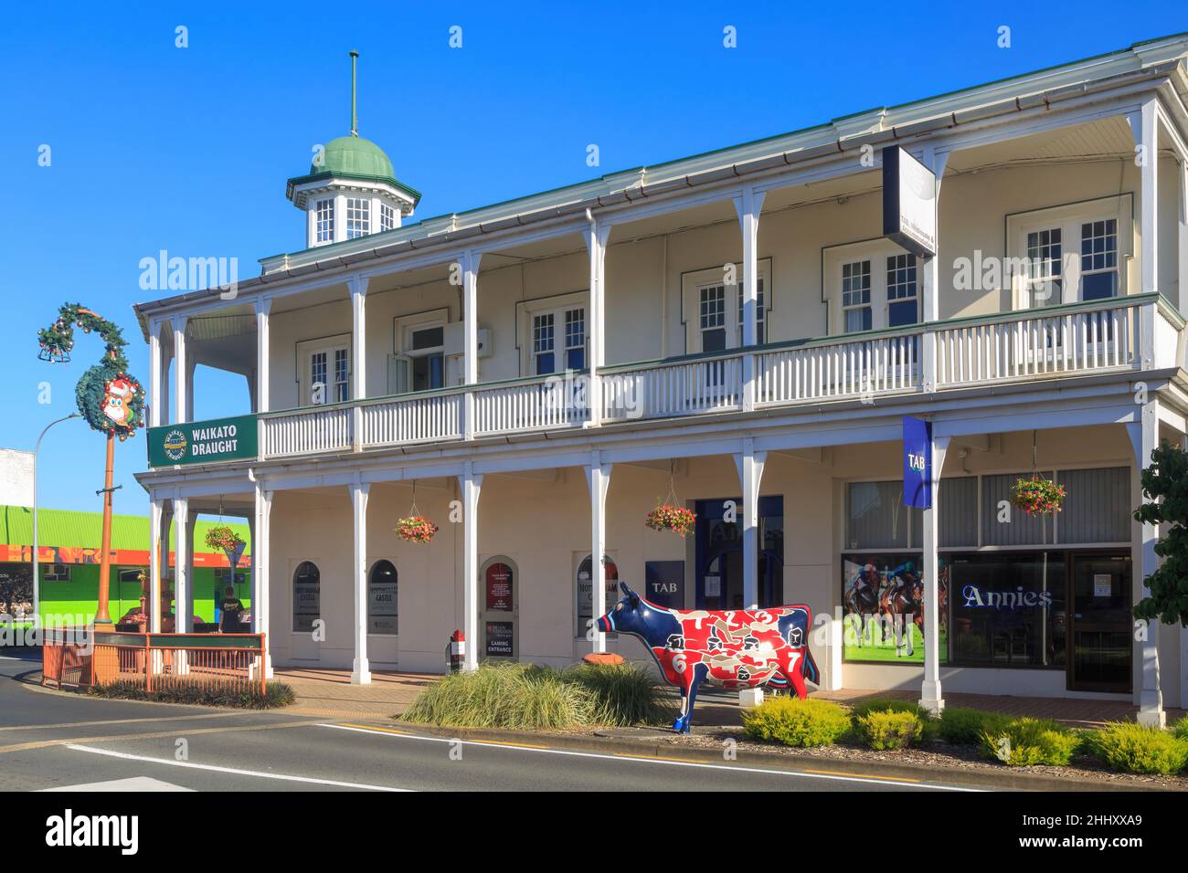Morrinsville, New Zealand. Nottingham Castle Hotel (1914), a historic building, with one of the town's many life-sized cow sculptures outside Stock Photo