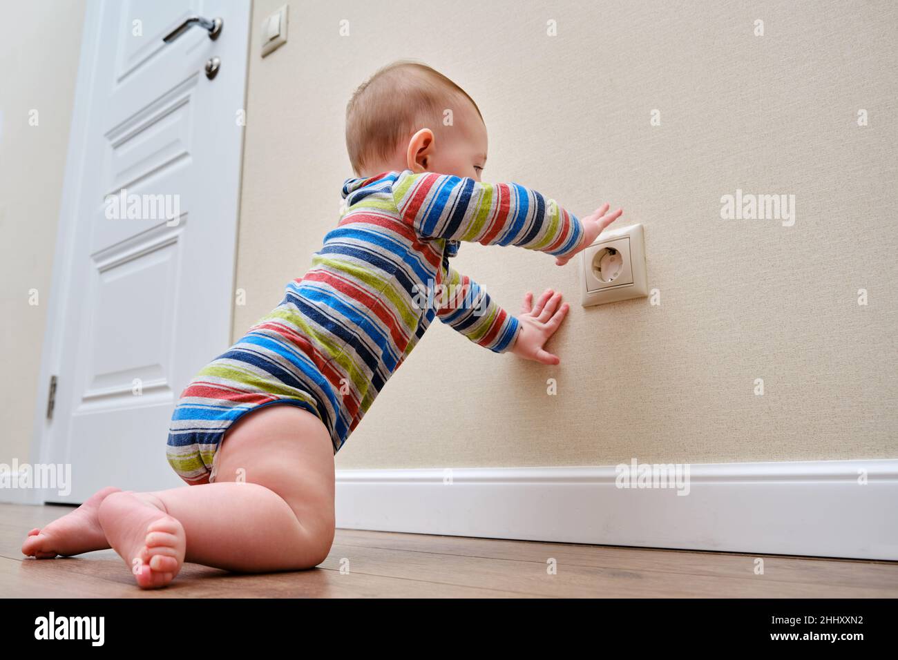 Baby toddler reaches into the electrical outlet on the home wall with