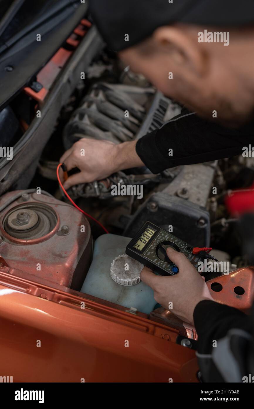 Hand of young repairman checking engine of car before repairing while bending over open hood and detecting reason of break Stock Photo
