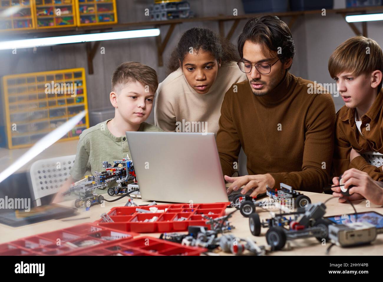 Group of children looking at monitor of laptop while teacher typing on ...