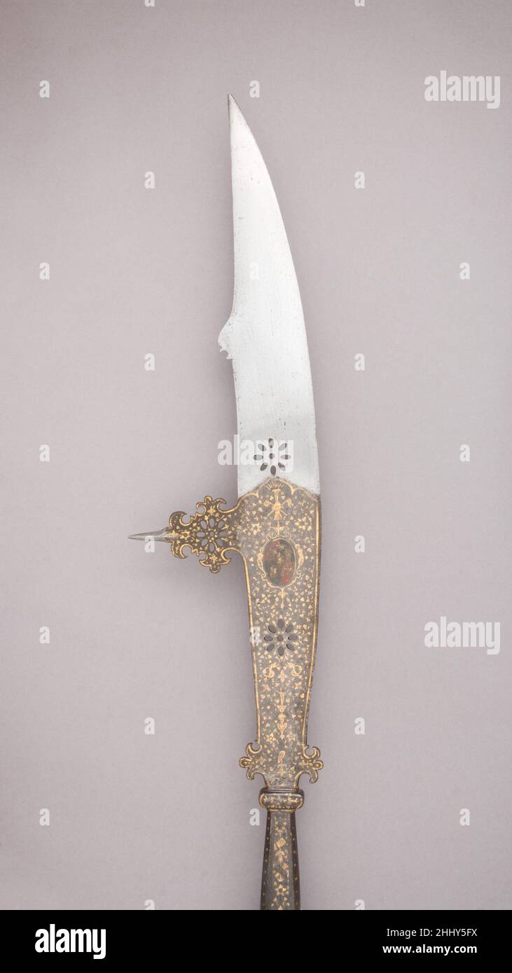 Fauchard ca. 1550 Italian, Venice Two rosettes pierce the long knife-like blade which has a spike set on a decoratively cut and pierced base at right angles to the back; between the blade and its socket are two trefoil-shaped lugs. The lower half of the blade, including the spike, is blued, chiseled, and damascened in gold; the decoration on each side includes flowers, grotesques, a sun, and a trophy composed of two conucopias and a flaming torch. An oval medallion on the right side is painted with the arms of the counts of Tiepolo, and that on the left side contains the arms of the counts of Stock Photo