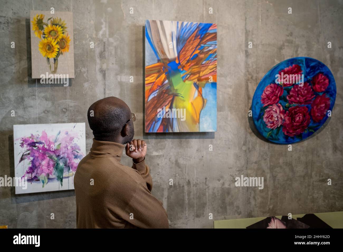 Rear view of African young man looking at colorful picture hanging on the wall while he visiting the exhibition Stock Photo