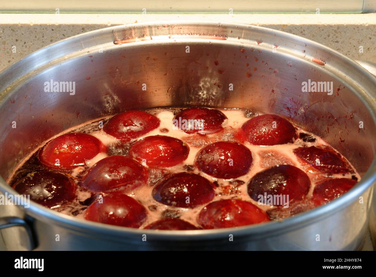 Plums cooking in a silver saucepan on oven hob. Cooking in syrup which