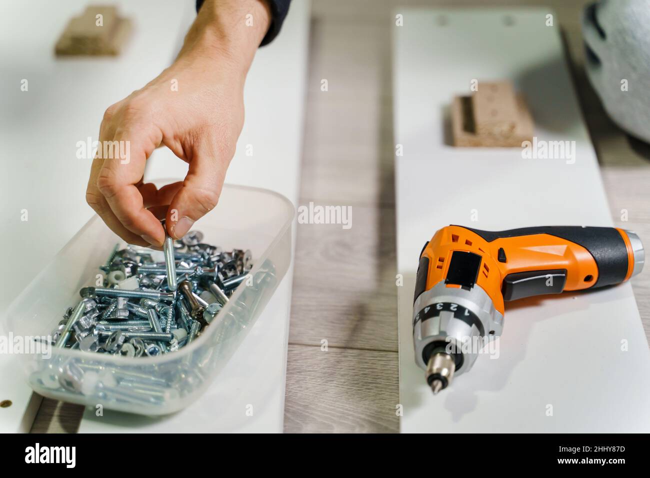 Close up on midsection of unknown caucasian man holding electric screwdriver while putting together Self assembly furniture of plywood screwing screws Stock Photo