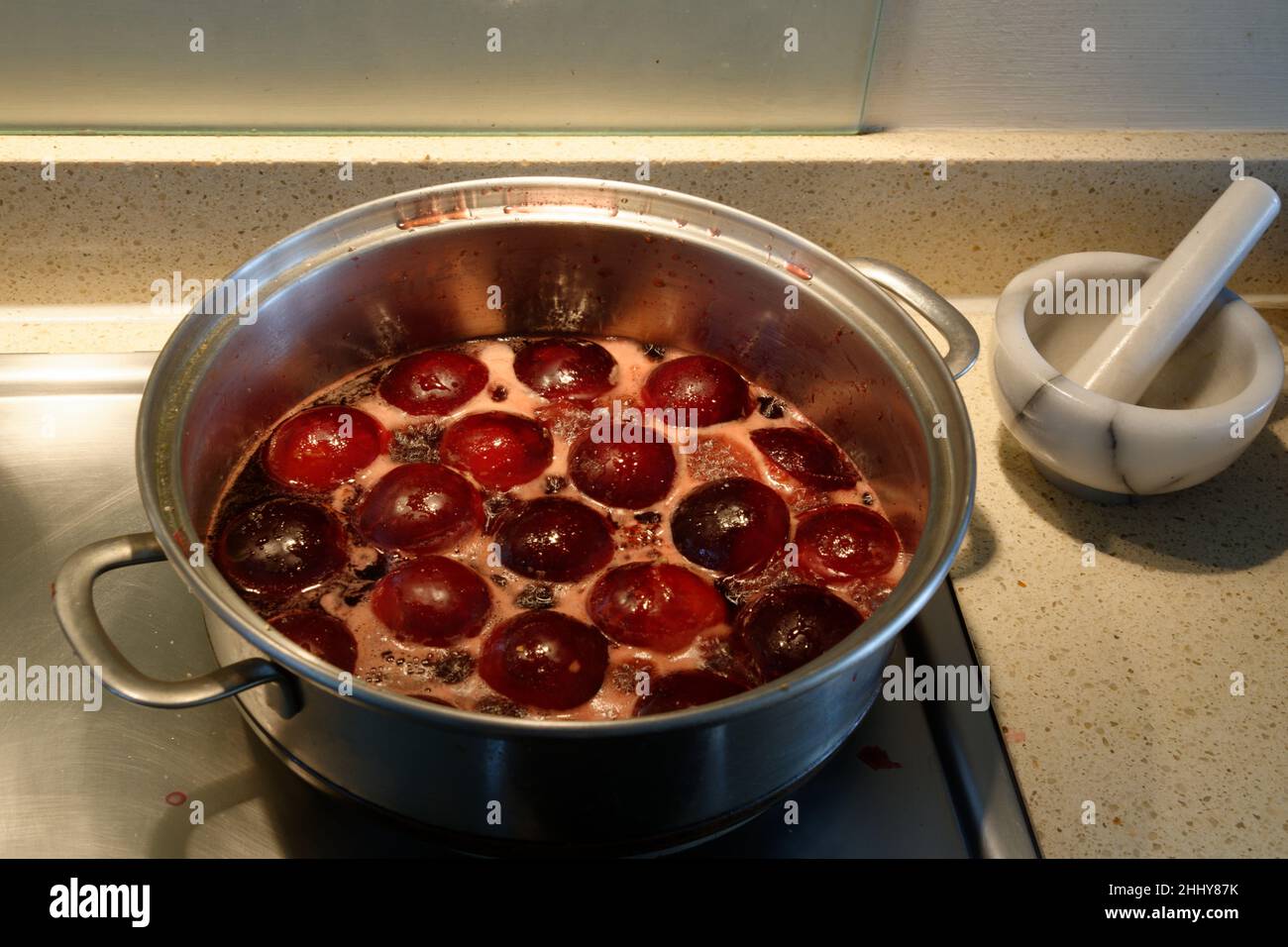 Plums cooking in a silver saucepan on oven hob. Cooking in syrup which