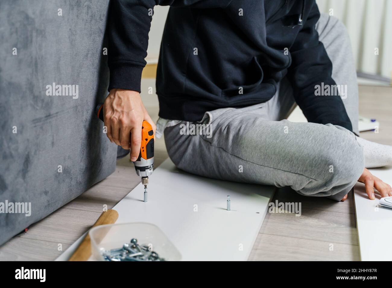 Close up on midsection of unknown caucasian man holding electric screwdriver while putting together Self assembly furniture of plywood screwing screws Stock Photo