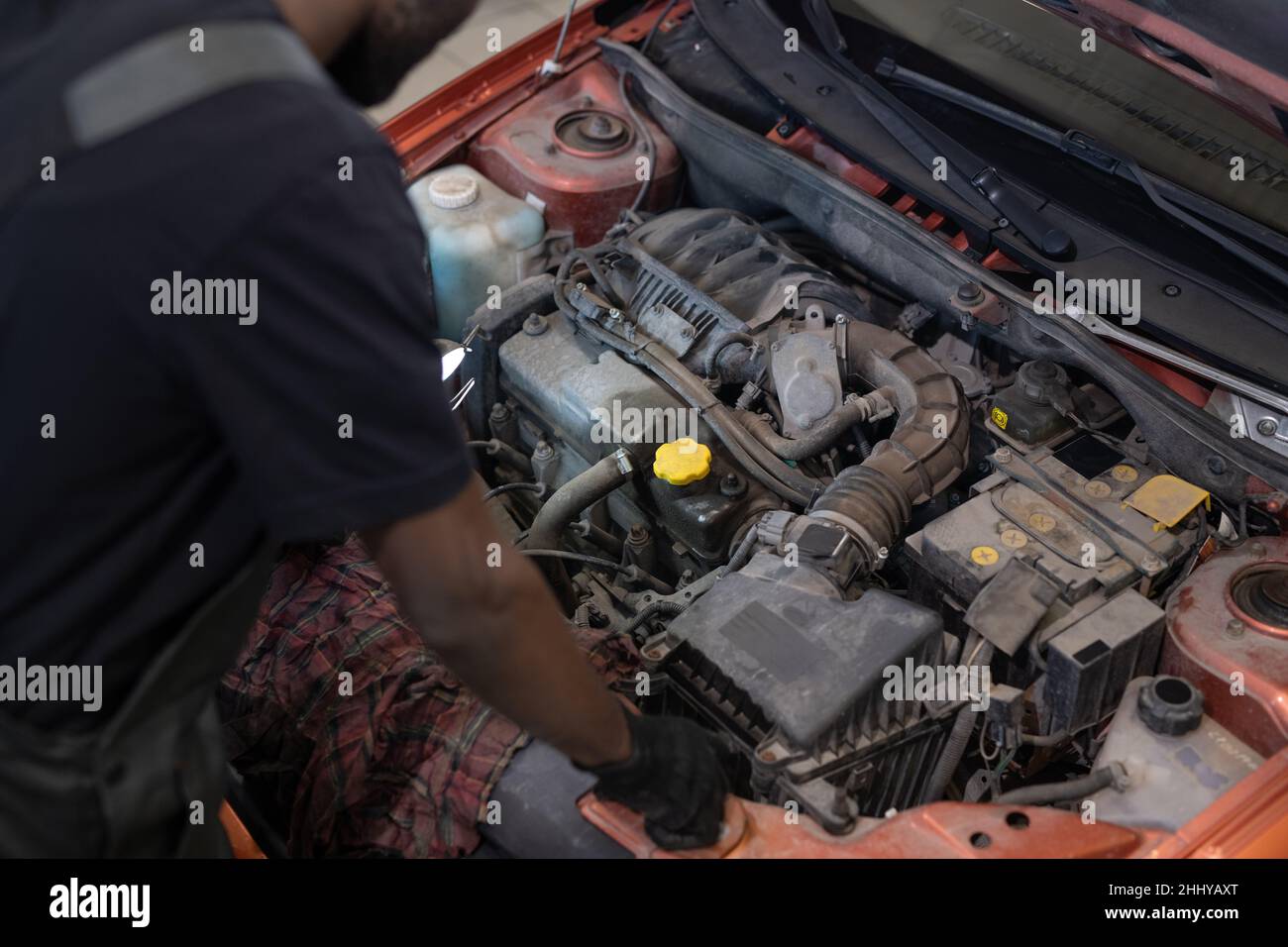 Part of young automechanic in workwear checking engine of car while standing by open hood with motor Stock Photo