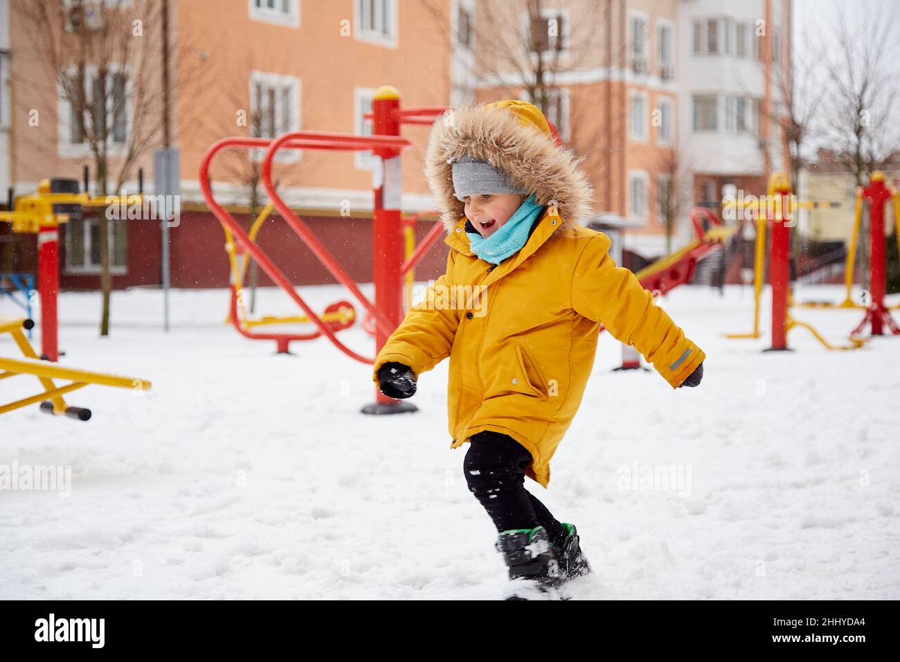 Happy smiling child having fun in the snow in the city. Winter fun outside. Boy in bright orange winter Jacket. Happy childhood. Winter season. High quality photo Stock Photo