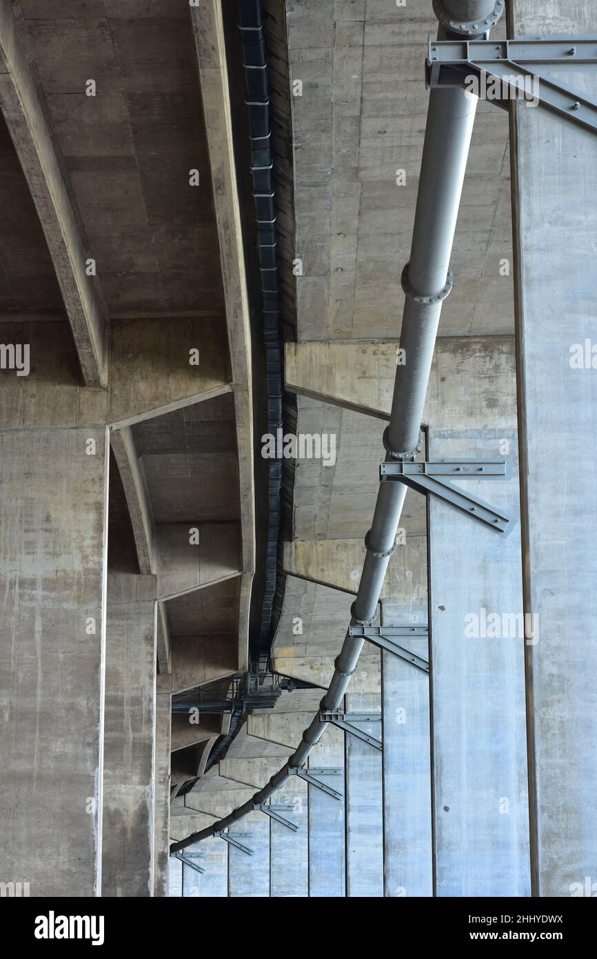 Big bore piping hanging under concrete structure of road bridge. Stock Photo