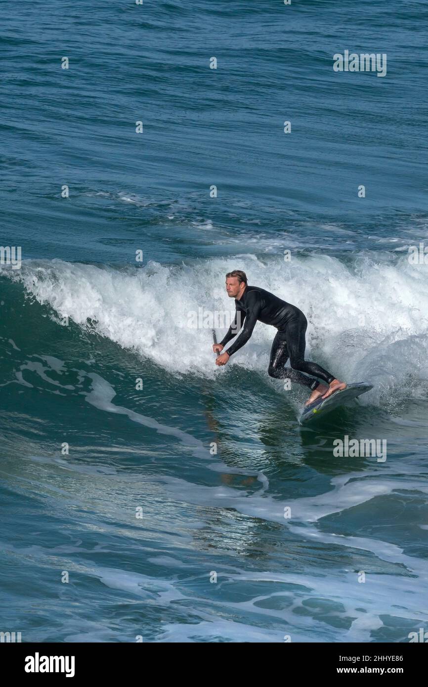 A determined Stand Up Paddleboarder riding a wave at Fistral in Newquay
