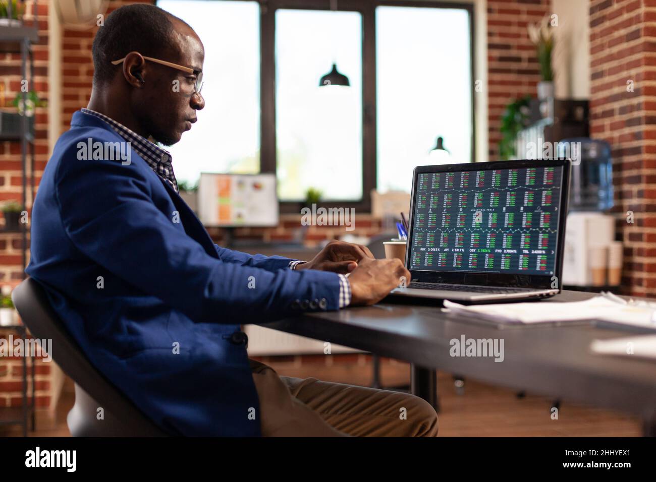 African american person using laptop with stock market numbers to invest in crypto currency. Employee analyzing data charts with global investment numbers to buy and sell money for profit. Stock Photo