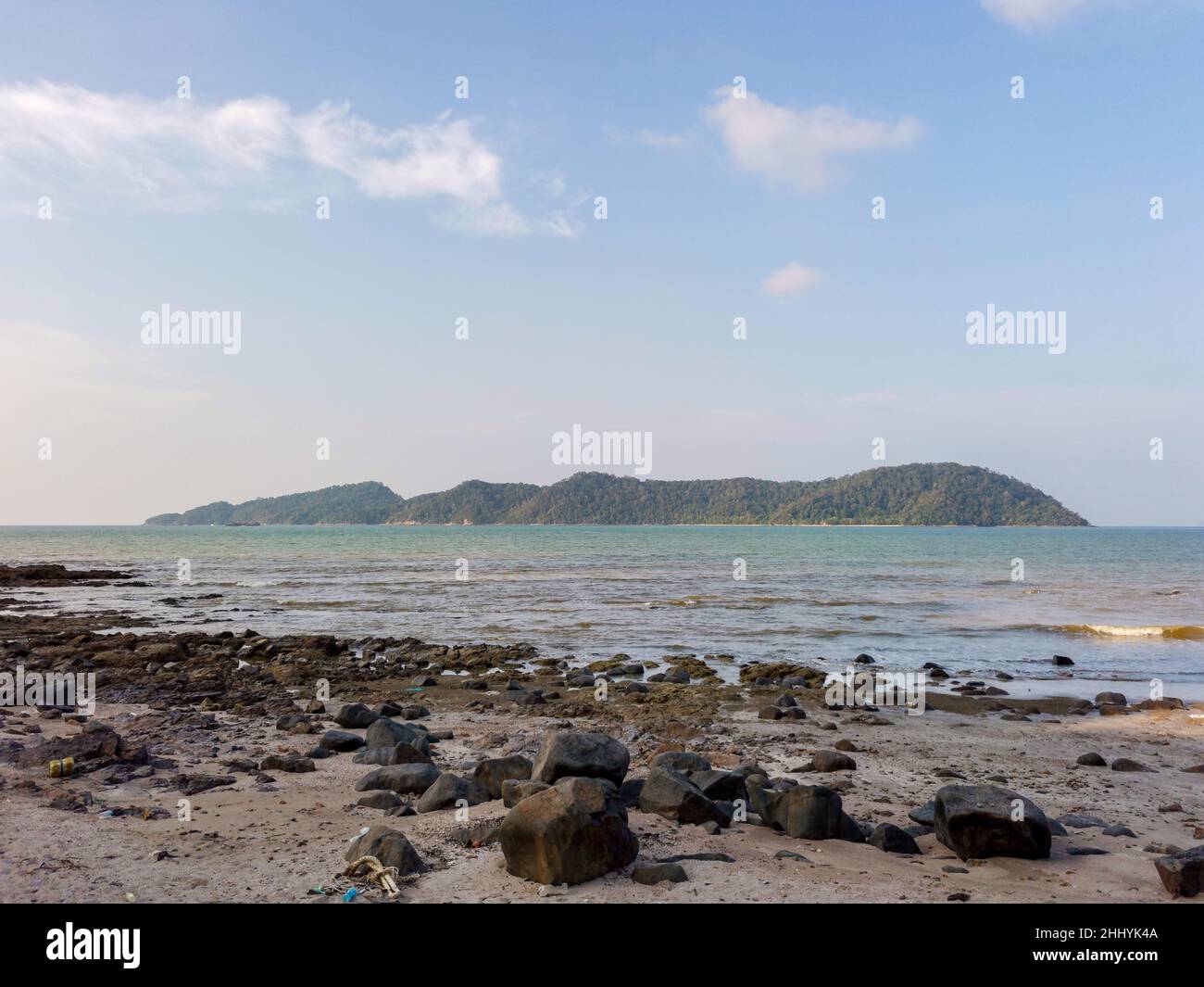 Seascape with boulders and sea waves lash line impact rock on a summer day. Beautiful tropical beach with blue sky and small island view at horizon. E Stock Photo