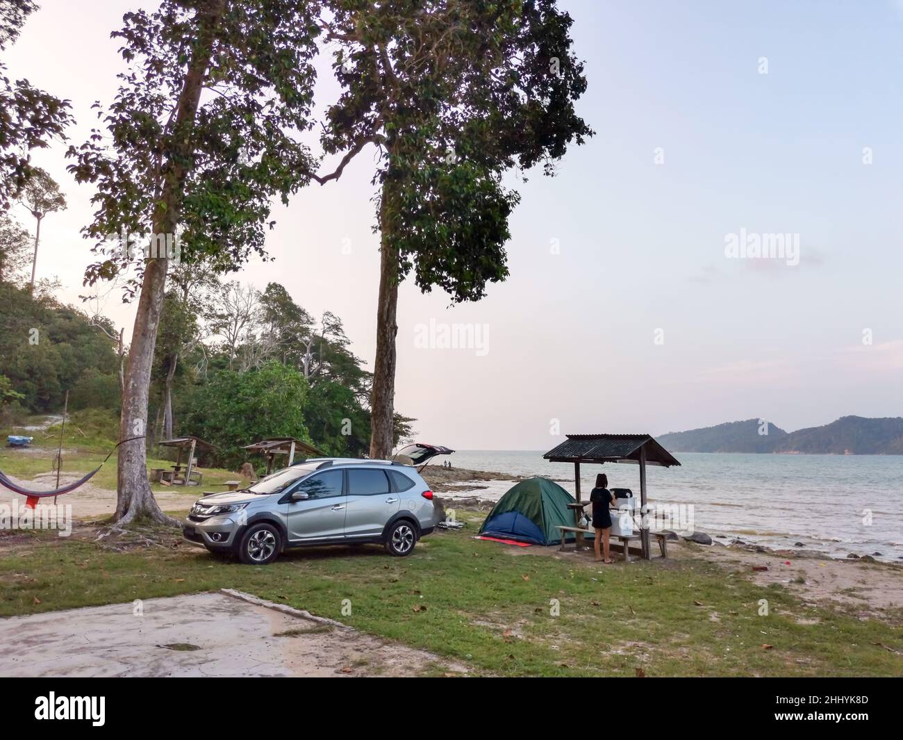 Camping and tent and SUV car under the pine tree near the seaside beach with sunset sky and small island at horizon. Endau, Malaysia Stock Photo