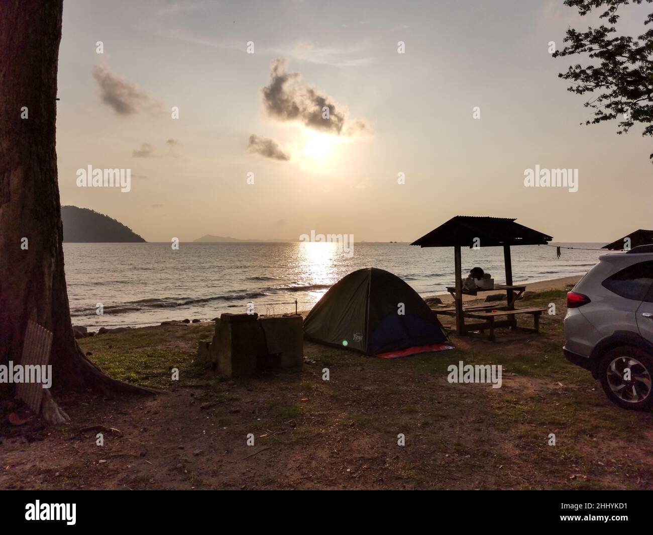 Camping with tent on the beach in the morning with golden sky and sunrise. Tent and picnic table during sunrise with sunlight on a sandy beach Stock Photo